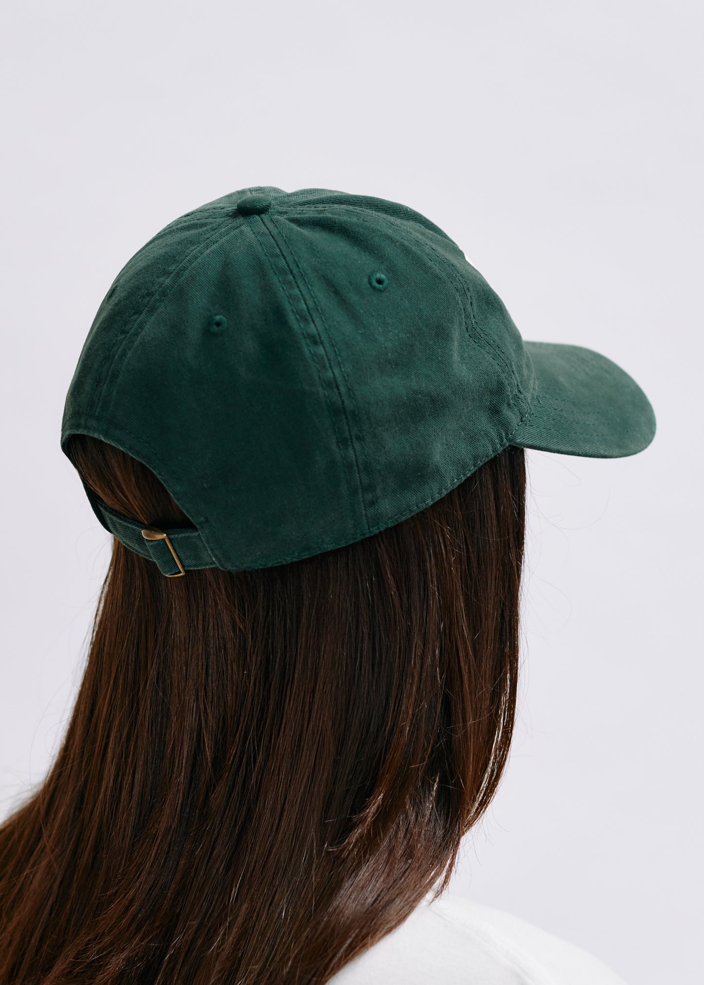 Green cap worn by a person with long hair on a light gray background