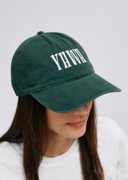 Green cap with 'YHWH' text worn by a person on a light gray background